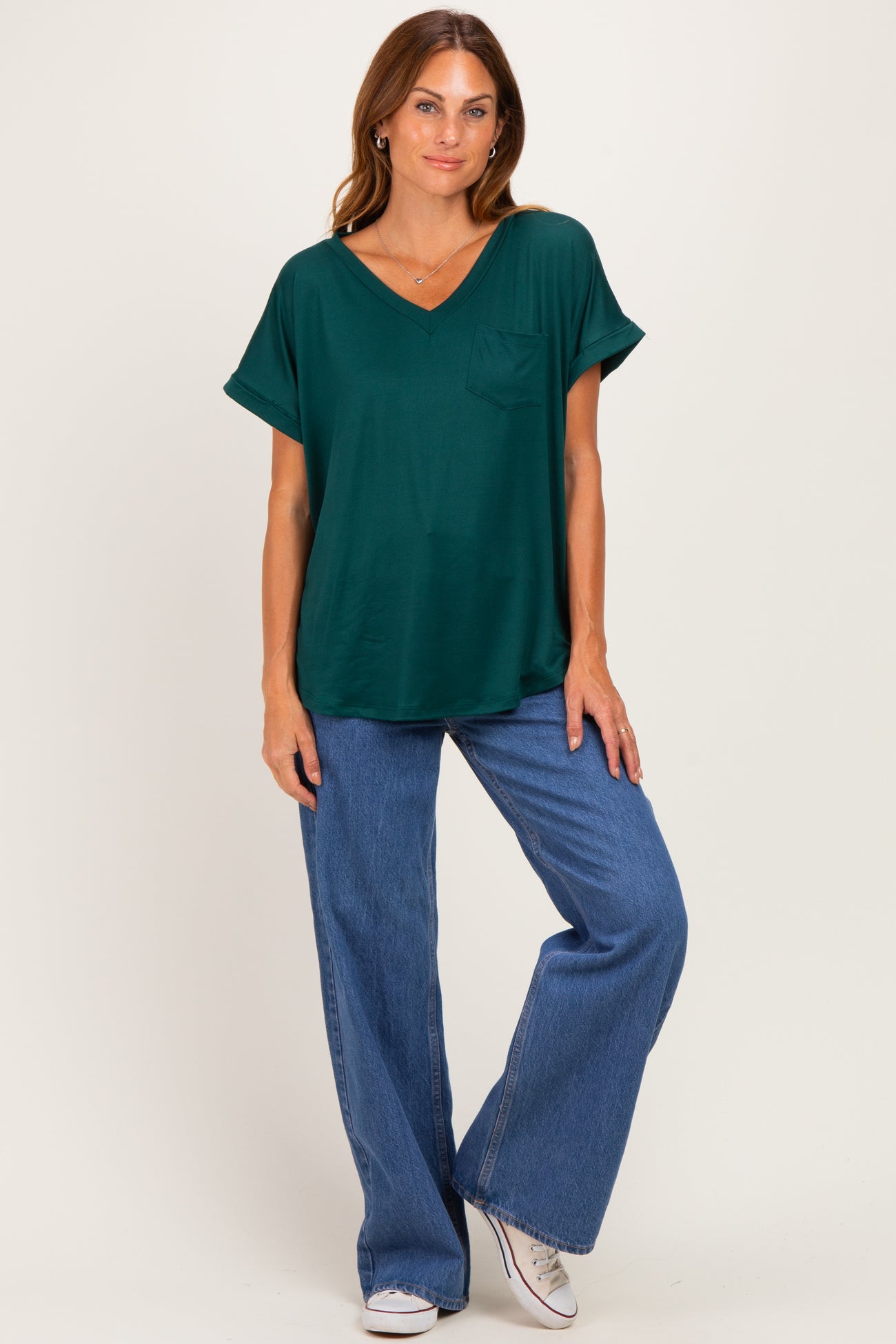 woman wearing a green short sleeve v-neck top with a pocket and blue wide-leg jeans