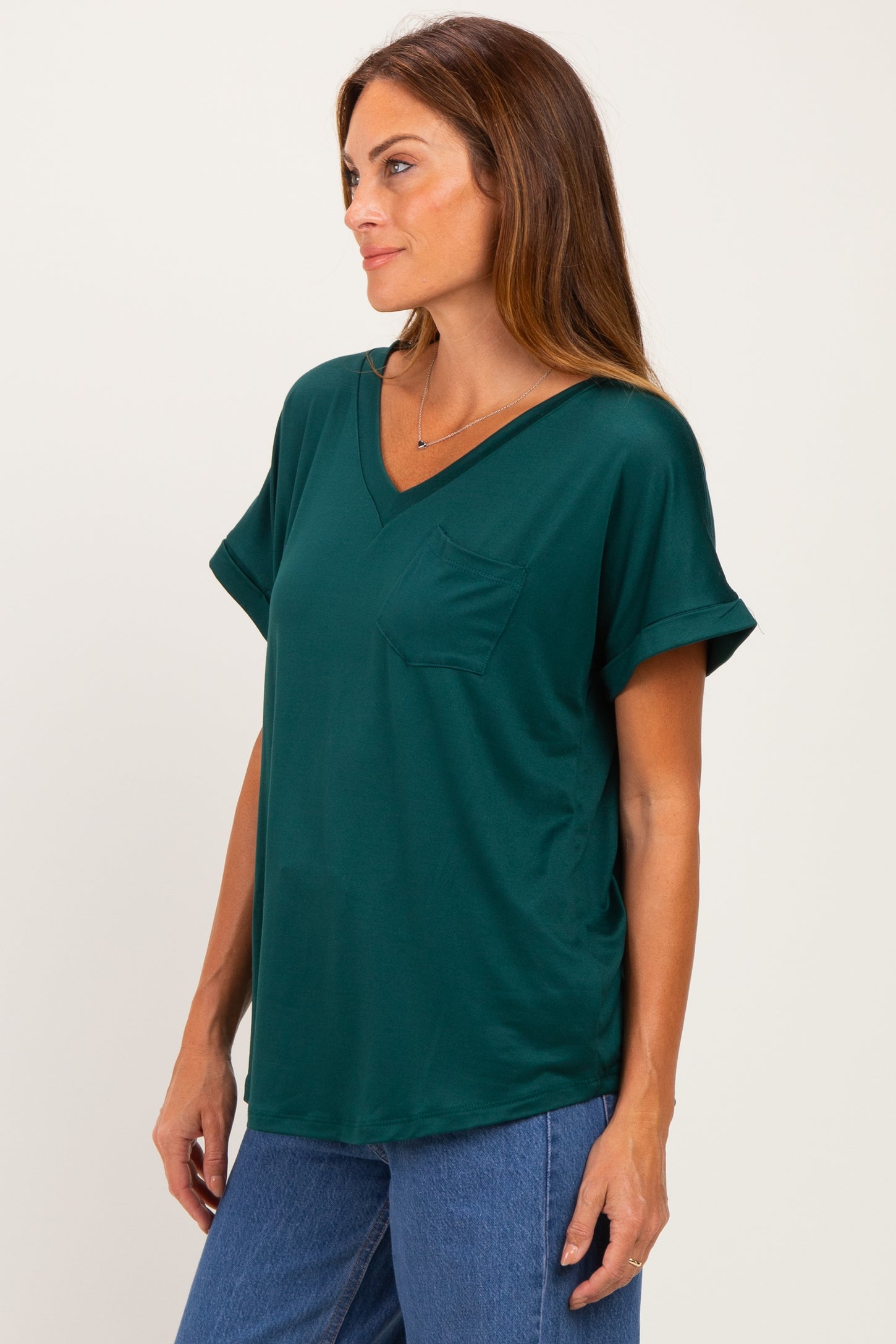 woman wearing a dark green v-neck short sleeve top with a chest pocket and styled with blue jeans