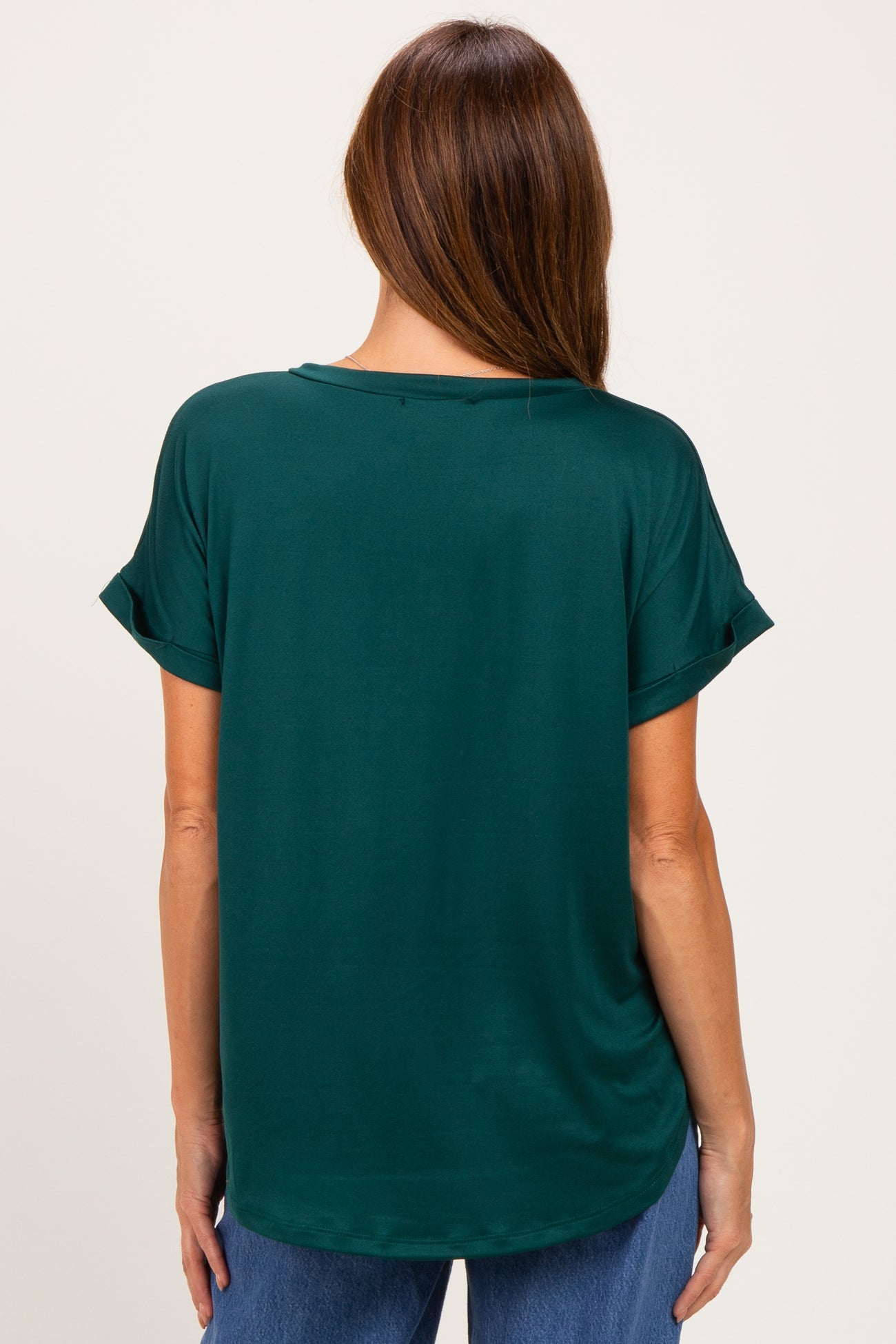 woman wearing a dark green short sleeve top, viewed from the back with a relaxed fit and rolled sleeves
