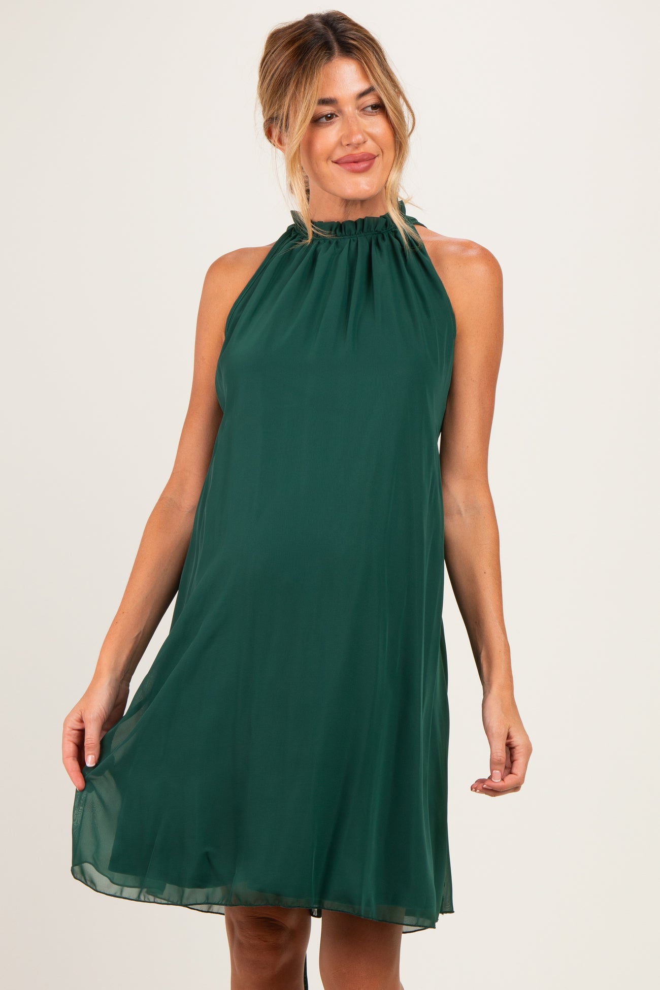woman wearing a dark green halter neck maternity dress with a flowy silhouette and gathered neckline