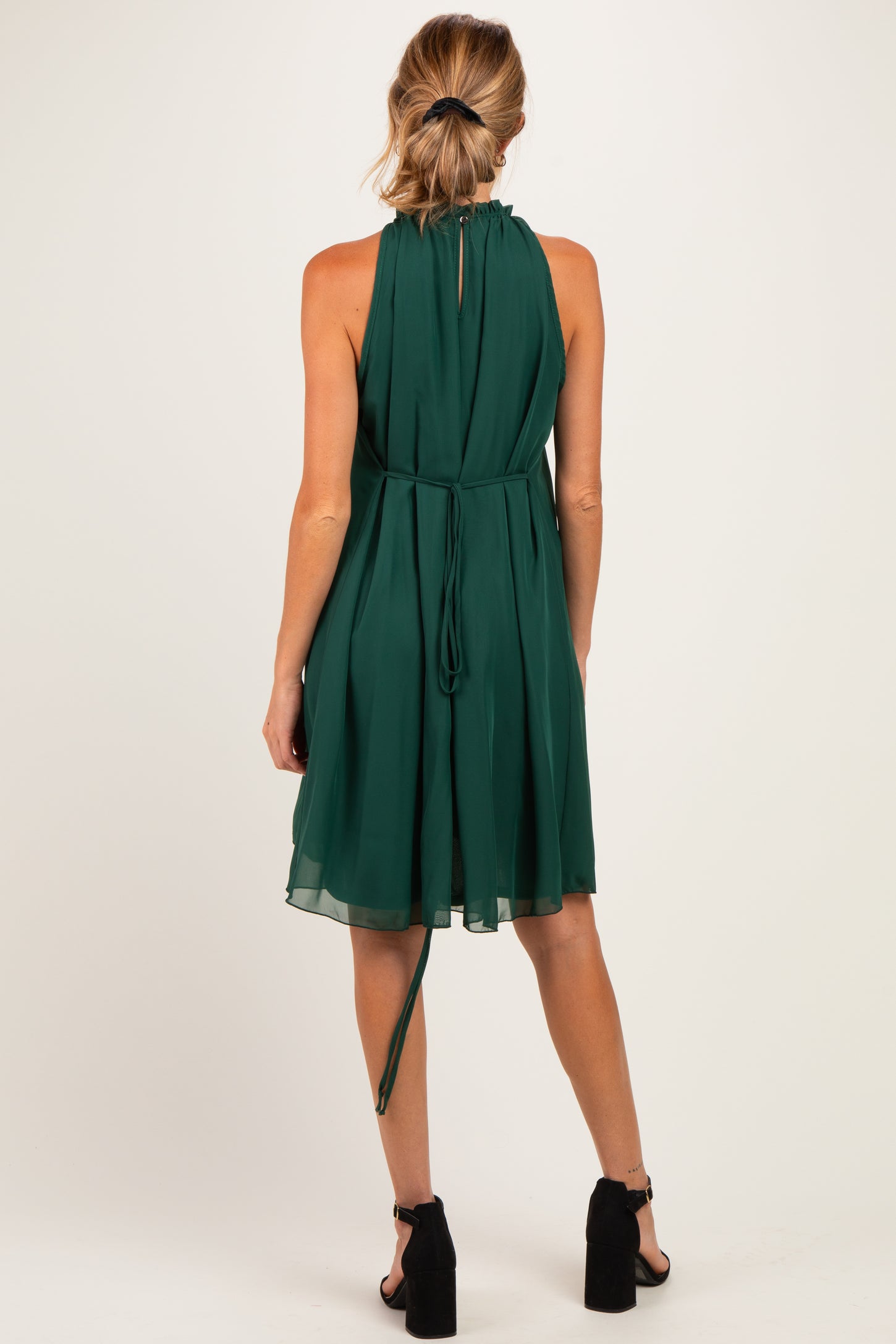 woman wearing a green maternity dress with a halter neck and a flowing skirt, showing a tied detail at the back
