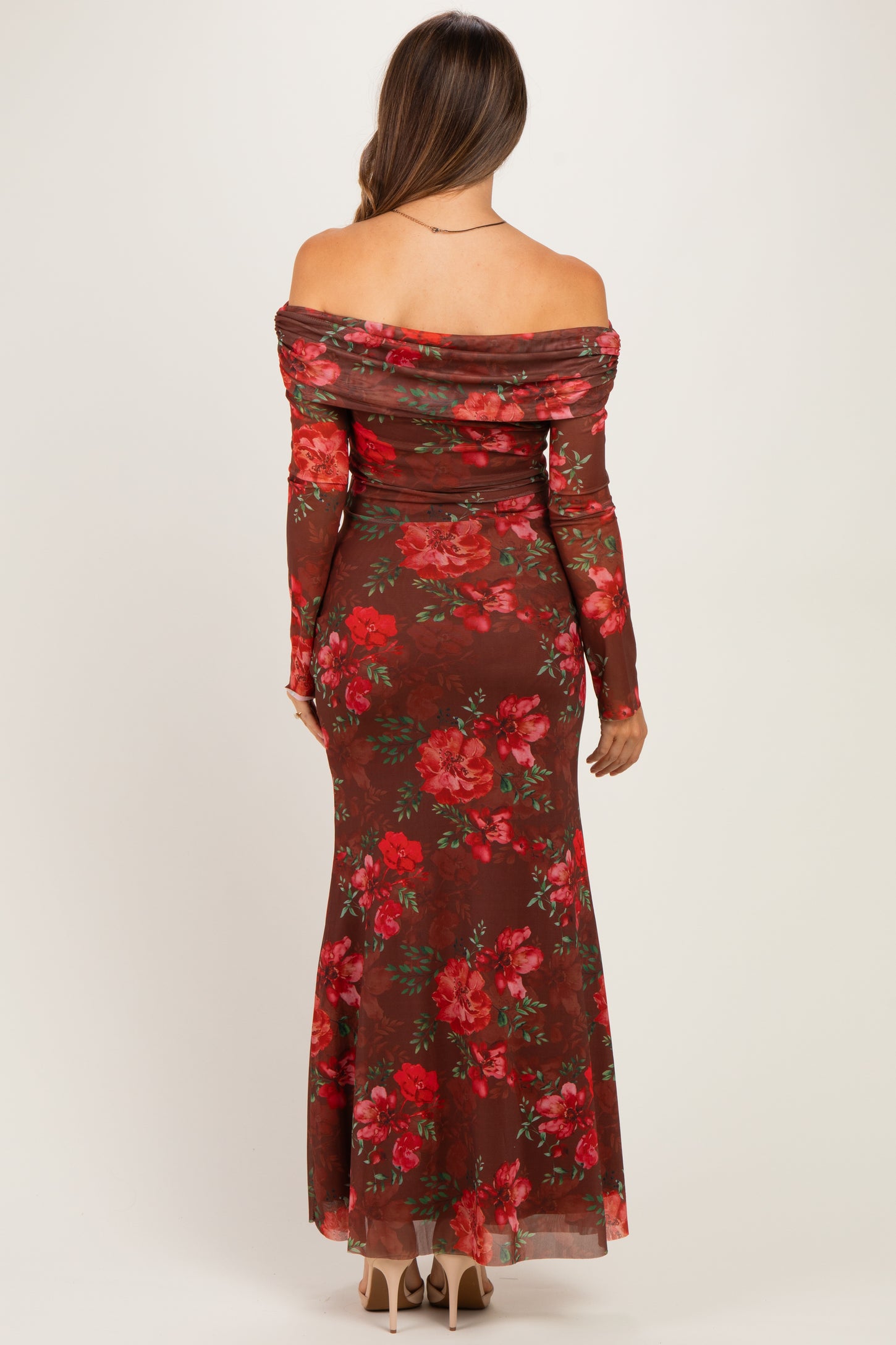 woman wearing a brown floral maternity gown with off-the-shoulder design and long sleeves, showing a baby bump