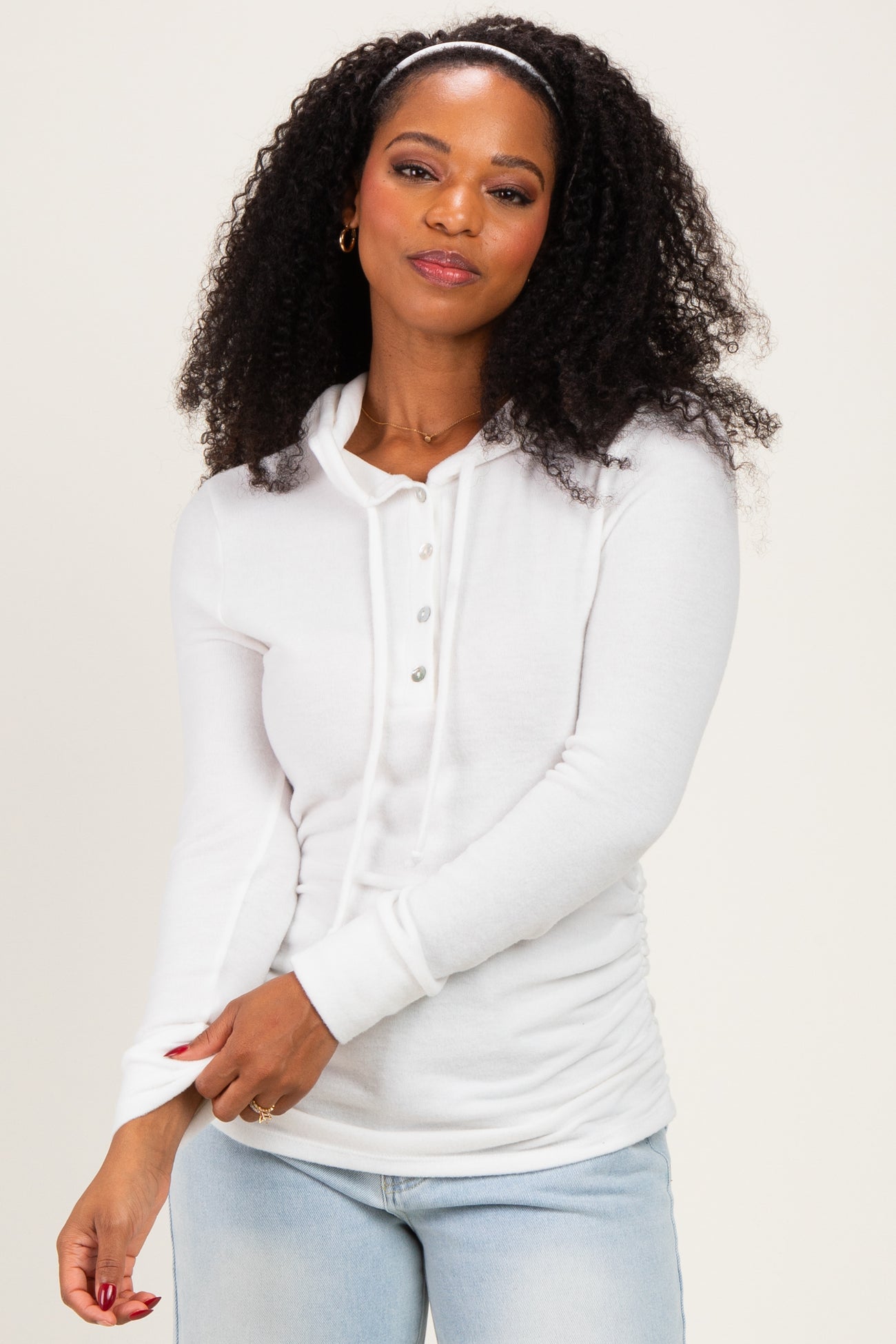 woman wearing a white long sleeve henley top with buttons and ruched sides, smiling at the camera