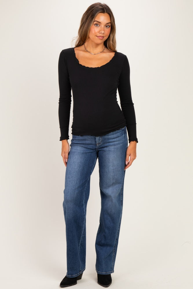 woman wearing a black long sleeve maternity top with scalloped neckline and blue straight leg jeans, showing her baby bump