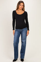 woman wearing a black long sleeve maternity top with scalloped neckline and blue straight leg jeans, showing her baby bump