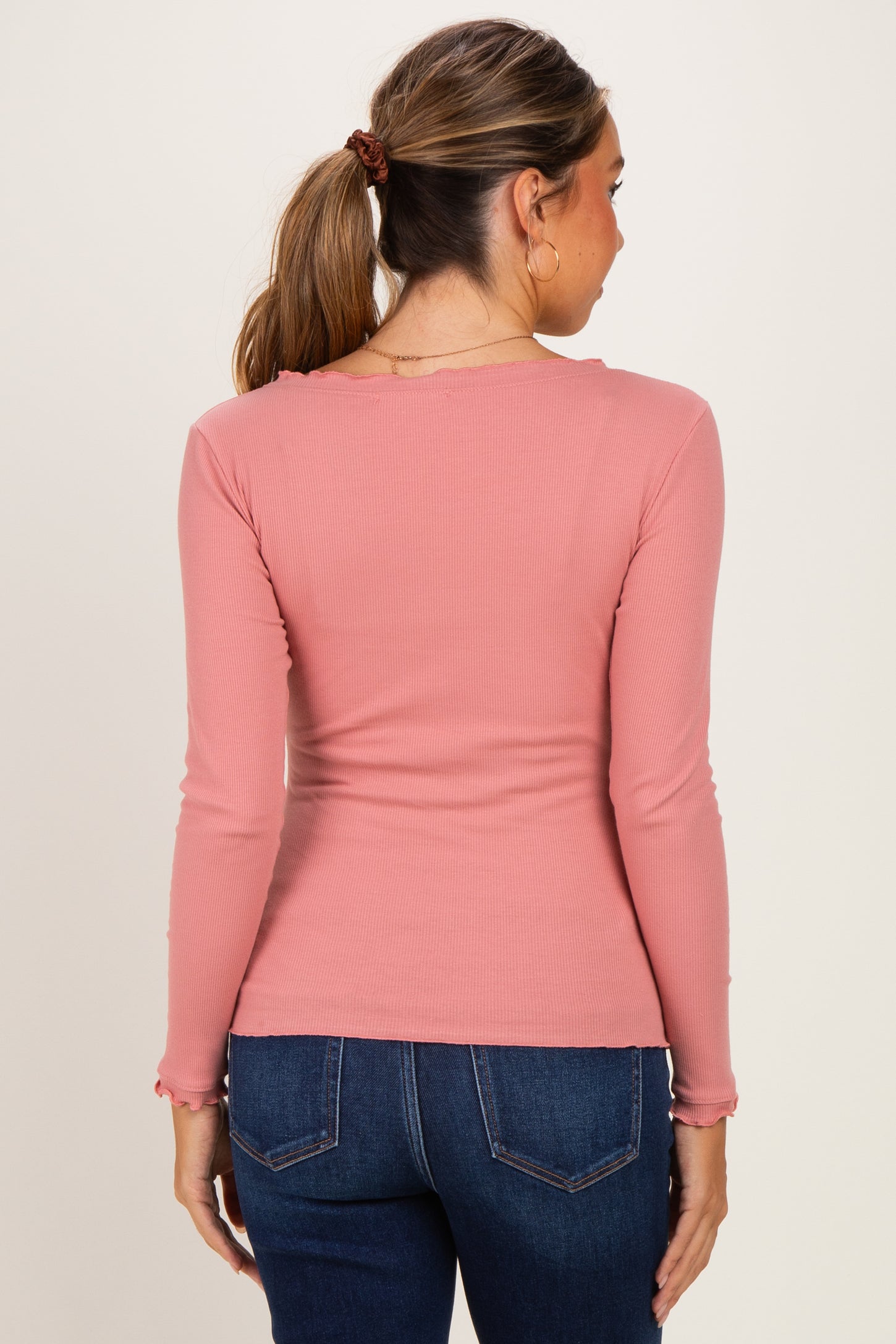 woman wearing a light pink long sleeve maternity top, viewed from the back, paired with dark blue jeans