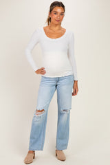 woman wearing a white long sleeve maternity top and distressed light blue jeans with a visible baby bump