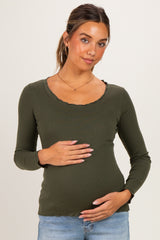 woman wearing an olive green long sleeve maternity top with a scalloped neckline and holding her baby bump