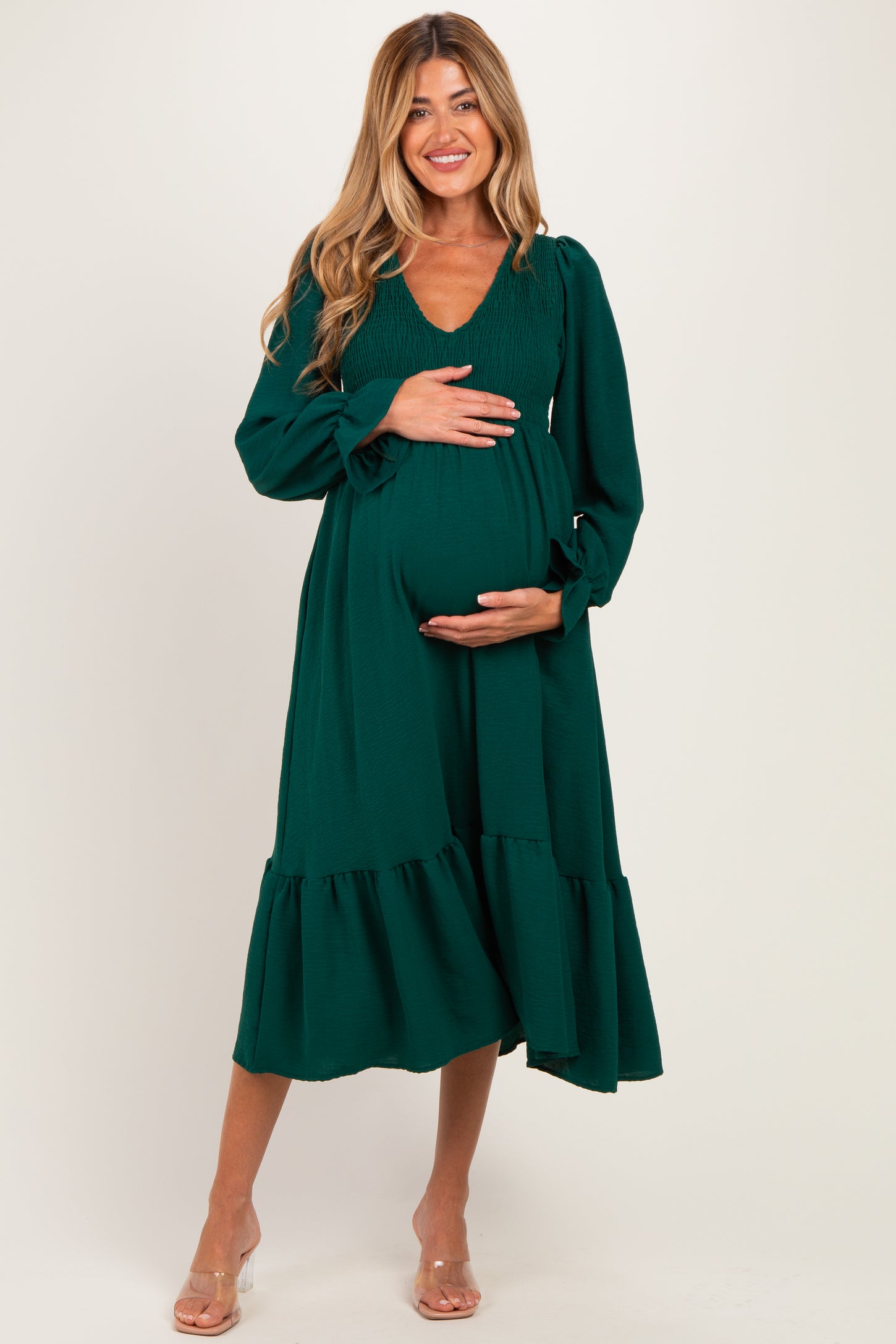woman wearing a green maternity dress with long sleeves and a ruffled hem, holding her baby bump