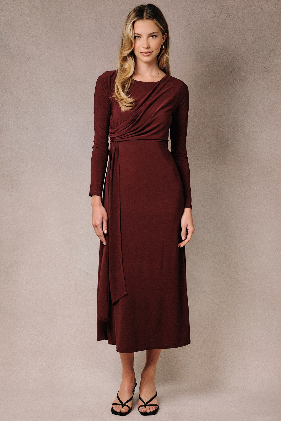 woman wearing a burgundy long sleeve wrap dress with a draped front and fitted silhouette