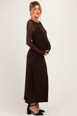 woman wearing a brown long sleeve maternity dress, cradling her baby bump
