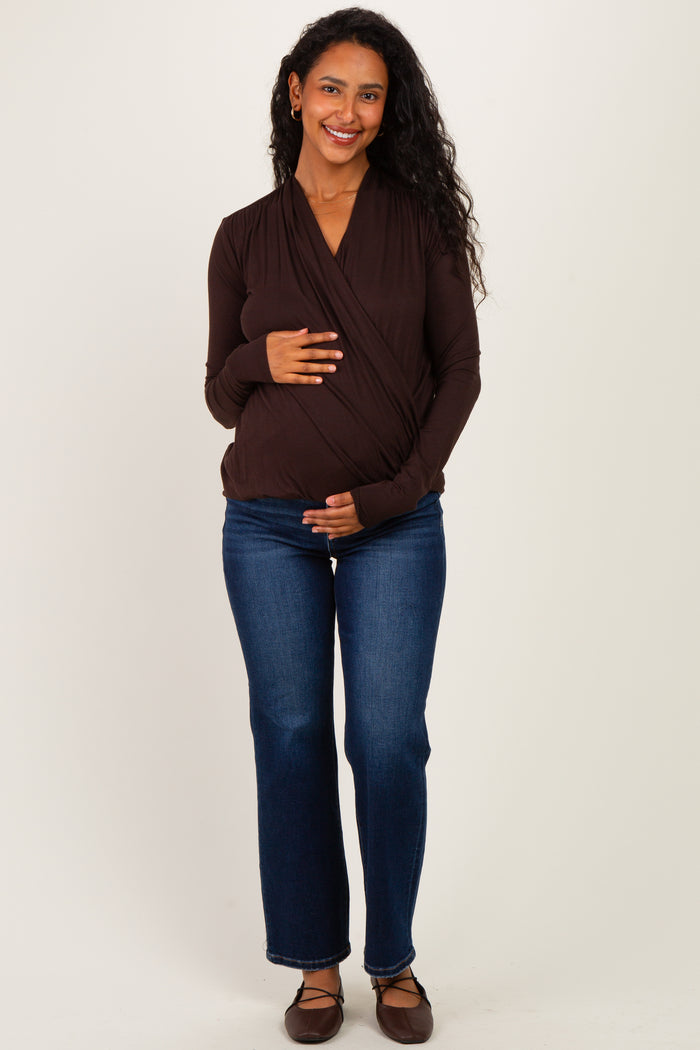 woman wearing a brown long sleeve maternity top and blue jeans, holding her baby bump