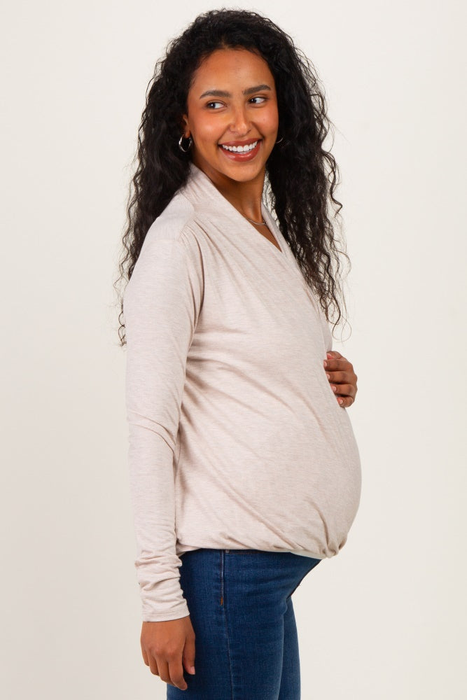 woman wearing a light beige long sleeve maternity top with a knotted detail and holding her baby bump