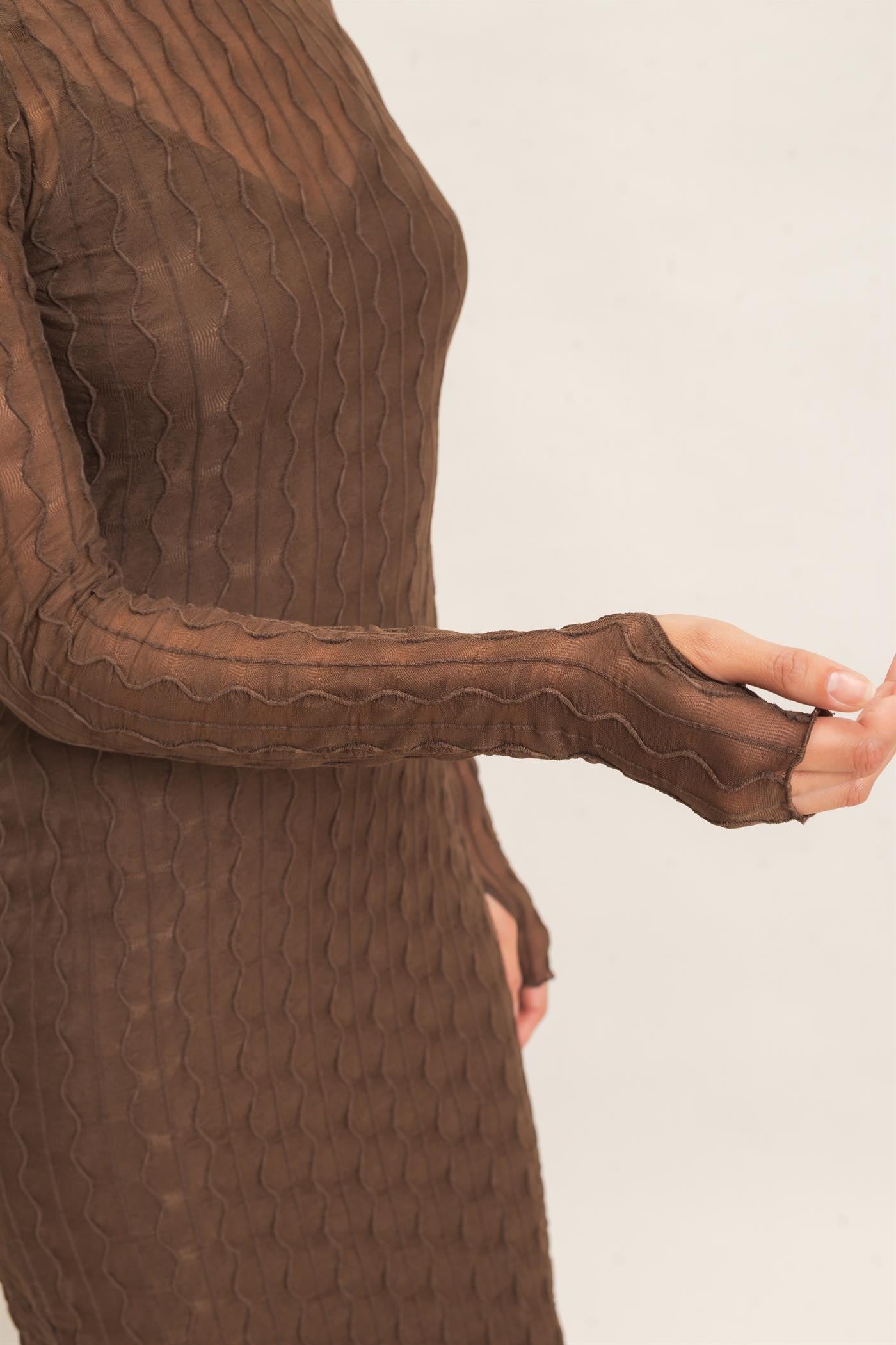 woman wearing a brown sheer long sleeve dress with a textured wavy pattern and thumbhole cuff details