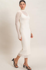 woman wearing a white fitted midi dress with sheer long sleeves and a scalloped hem, styled with black strappy heels
