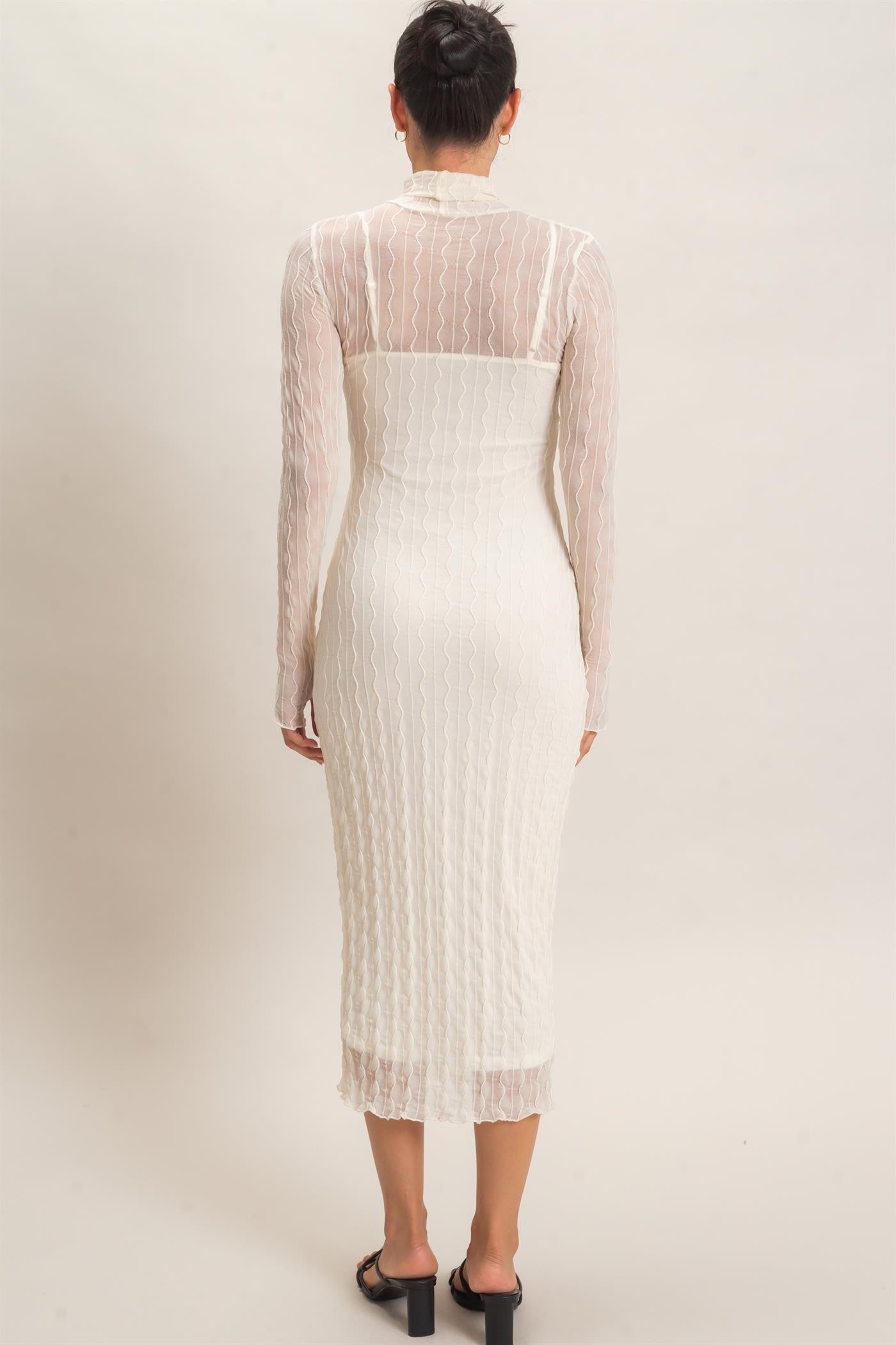 woman wearing a white long sleeve midi dress with a fitted silhouette and textured detailing, viewed from the back