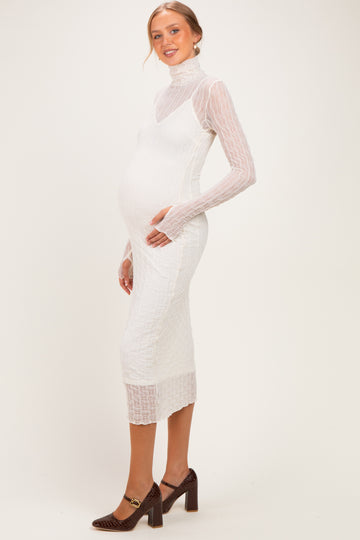 woman wearing a white maternity dress with a textured overlay and long sleeves, showing her baby bump