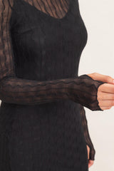 woman wearing a black long sleeve dress with textured wave patterns and sheer sleeves
