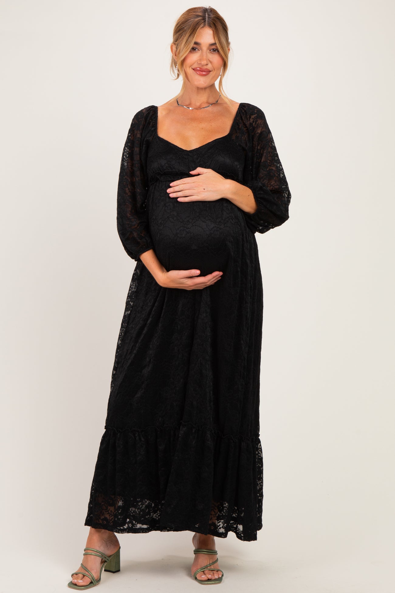 woman wearing a black lace long sleeve maternity dress and holding her baby bump