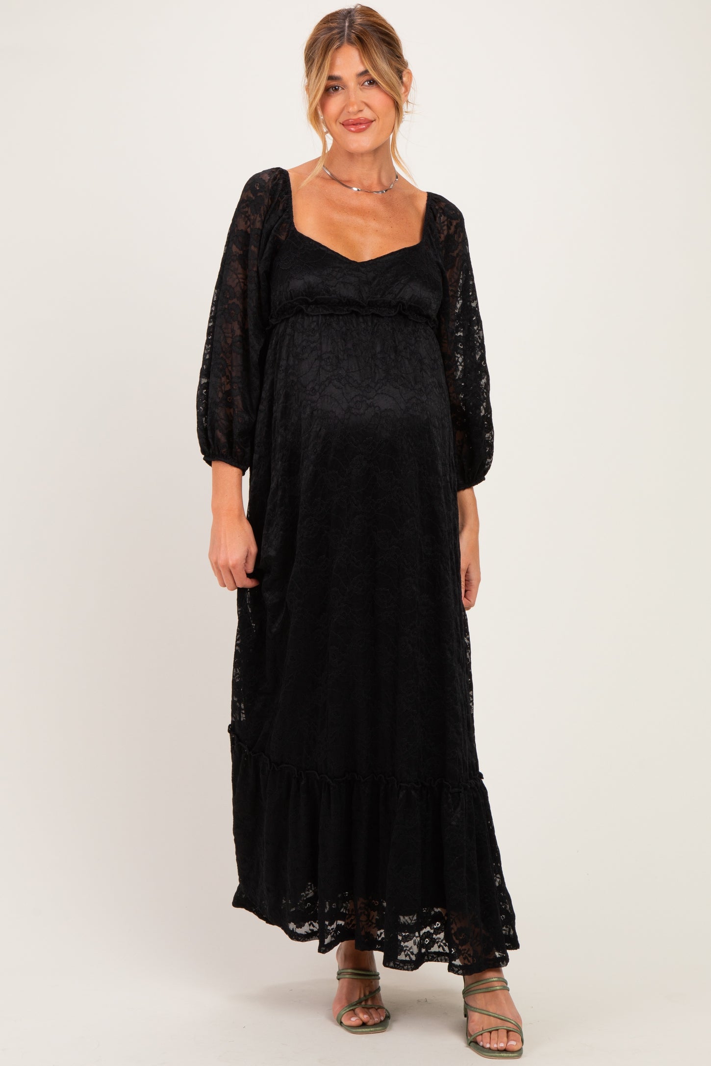 woman wearing a black lace maternity maxi dress with a tiered hem and balloon sleeves, showing her baby bump