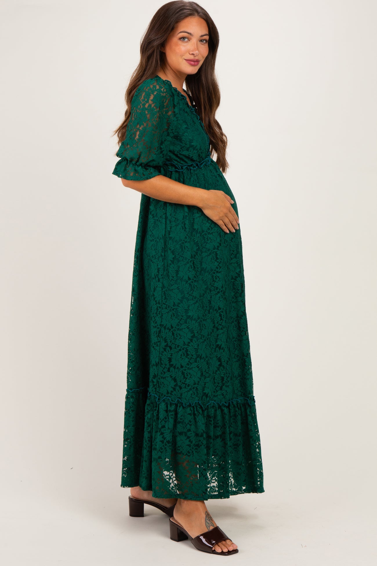 woman wearing a green lace maternity maxi dress and holding her baby bump