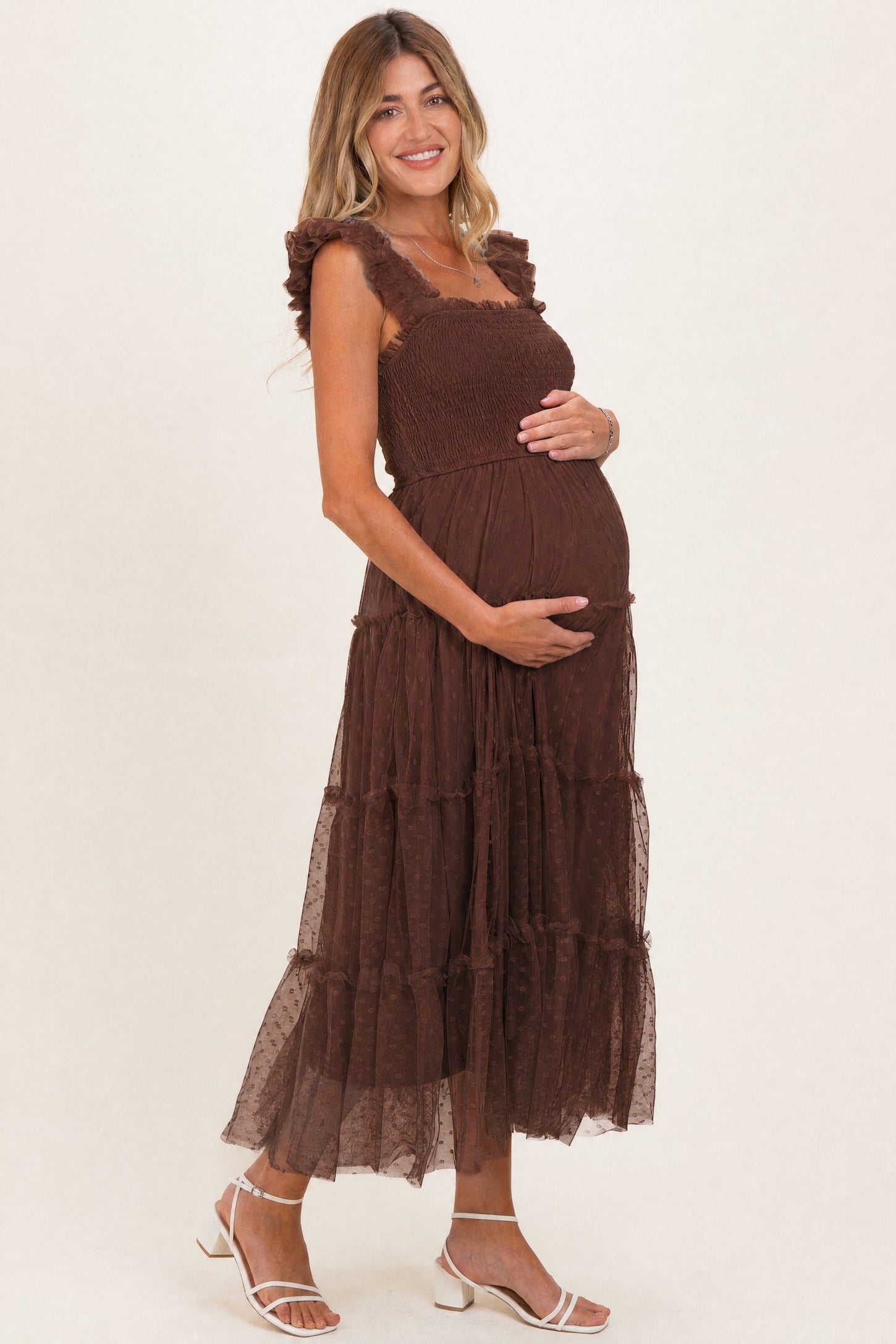 woman wearing a brown tiered maternity dress with ruffle straps and holding her baby bump