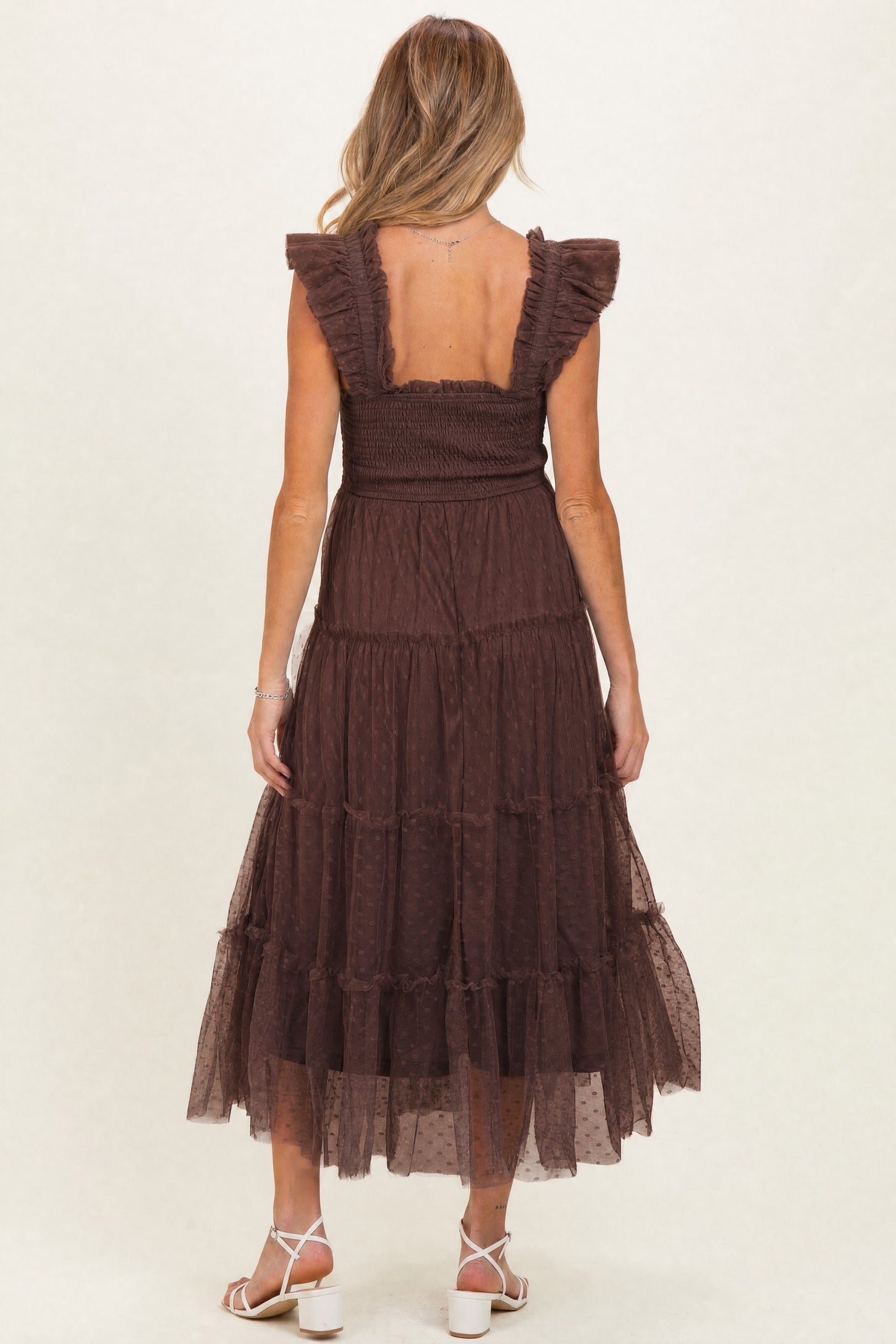 woman wearing a chocolate brown maternity maxi dress with ruffled sleeves and a tiered skirt, showing her back