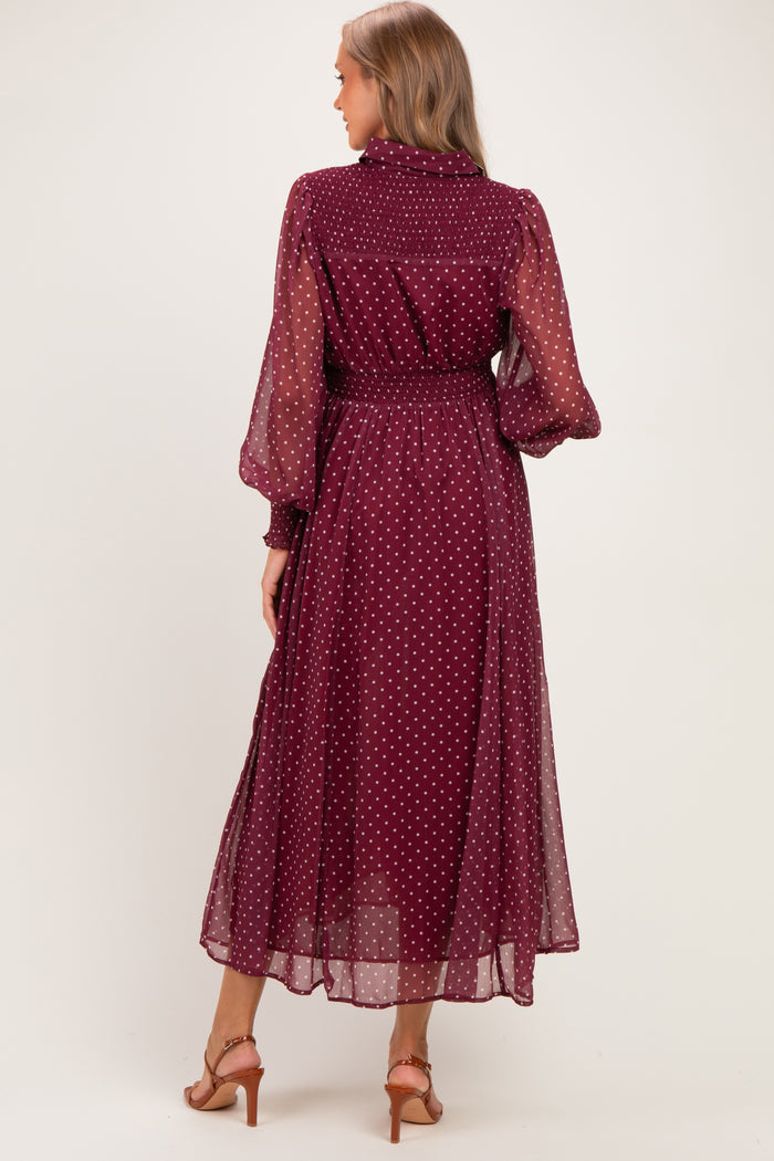 woman wearing a burgundy polka dot maternity dress with long sheer sleeves and a cinched waist, seen from the back