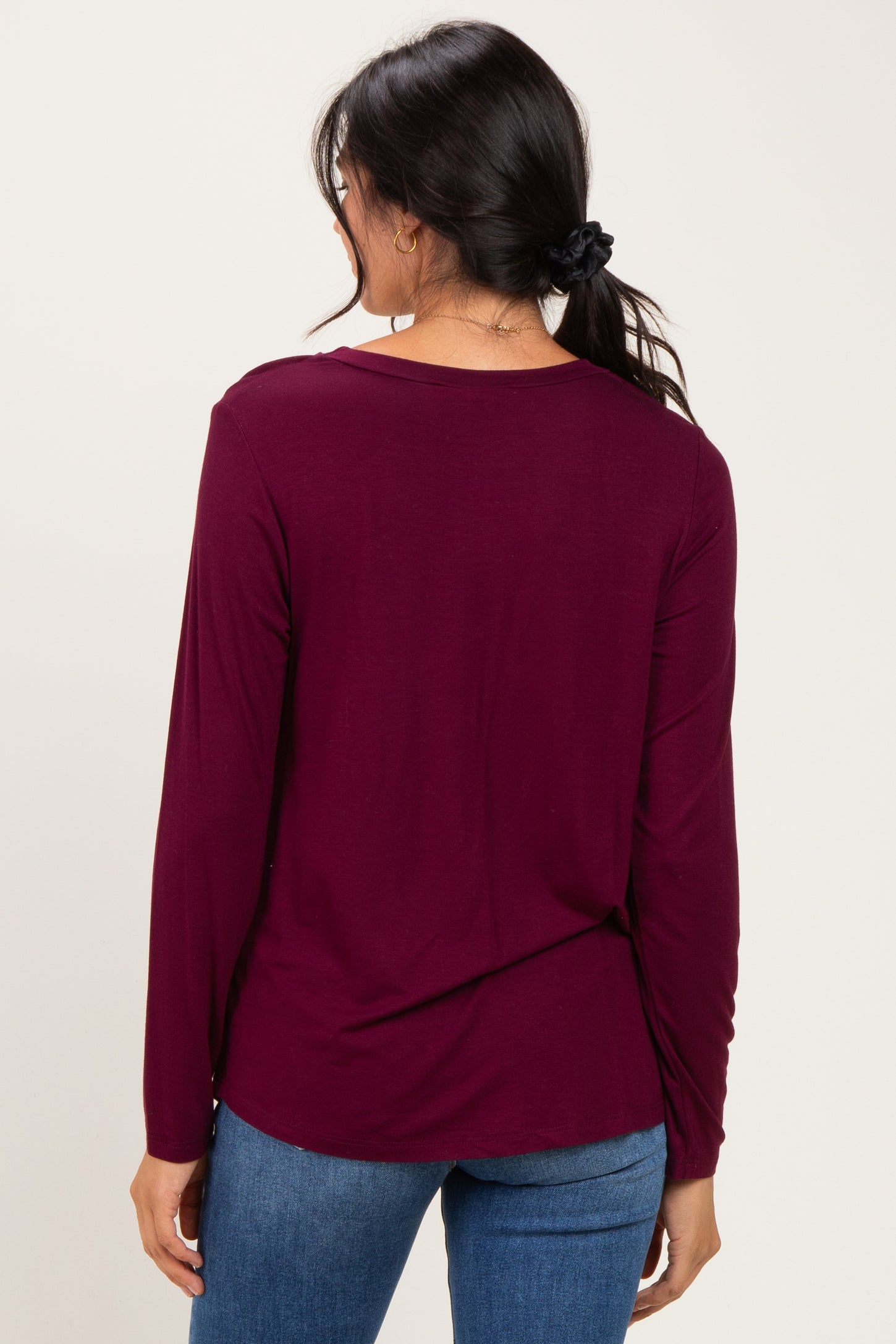 woman wearing a burgundy long sleeve top, viewed from the back, paired with blue jeans