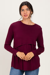woman wearing a burgundy long sleeve top with a layered design and relaxed fit, posing against a plain background