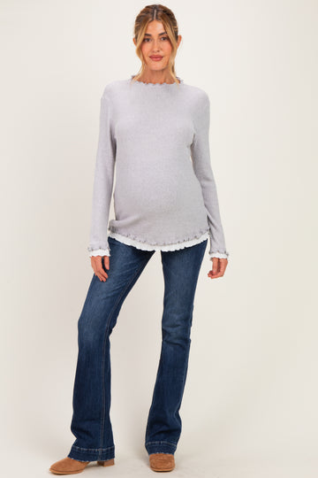 woman wearing a light gray maternity sweater with scalloped hem and long sleeves, paired with blue flared jeans and a visible baby bump