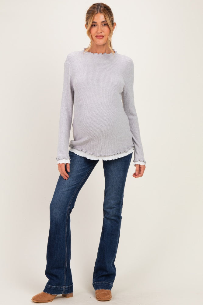 woman wearing a light gray maternity sweater with scalloped hem and long sleeves, paired with blue flared jeans and a visible baby bump