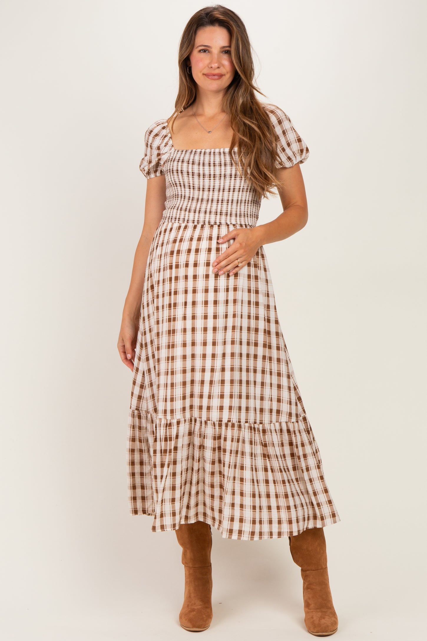 woman wearing a brown and white checkered midi maternity dress and holding her baby bump