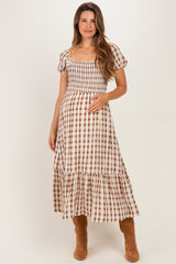 woman wearing a brown and white checkered midi maternity dress and holding her baby bump