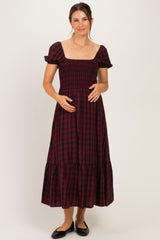 woman wearing a burgundy checkered maternity dress with short puff sleeves and a tiered skirt, holding her baby bump