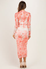 woman wearing a coral floral lace maternity dress with long sleeves, showing a fitted silhouette and knee-length hem