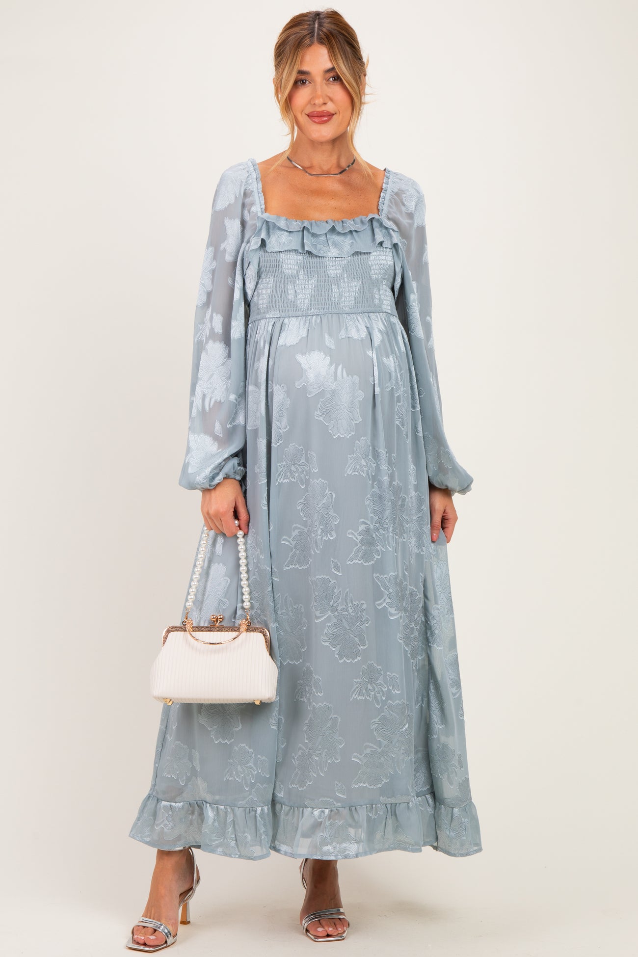 woman wearing a light blue floral maternity maxi dress with long sleeves and a baby bump, holding a handbag
