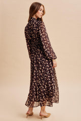 woman wearing a black floral maxi dress with long sleeves and back ruching, styled with nude heels