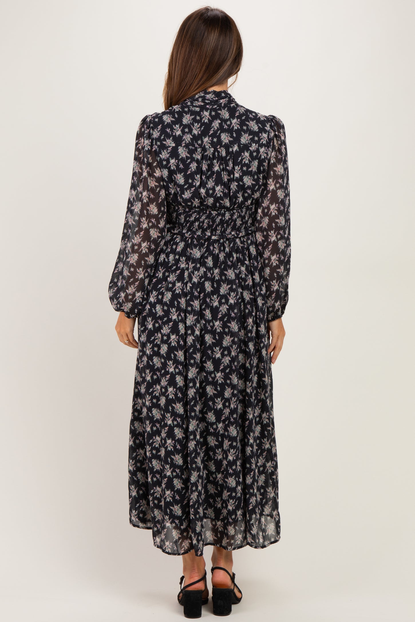 woman wearing a black floral maternity dress with long sleeves and a cinched waist, standing from the back