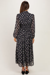 woman wearing a black floral maternity dress with long sleeves and a cinched waist, standing from the back