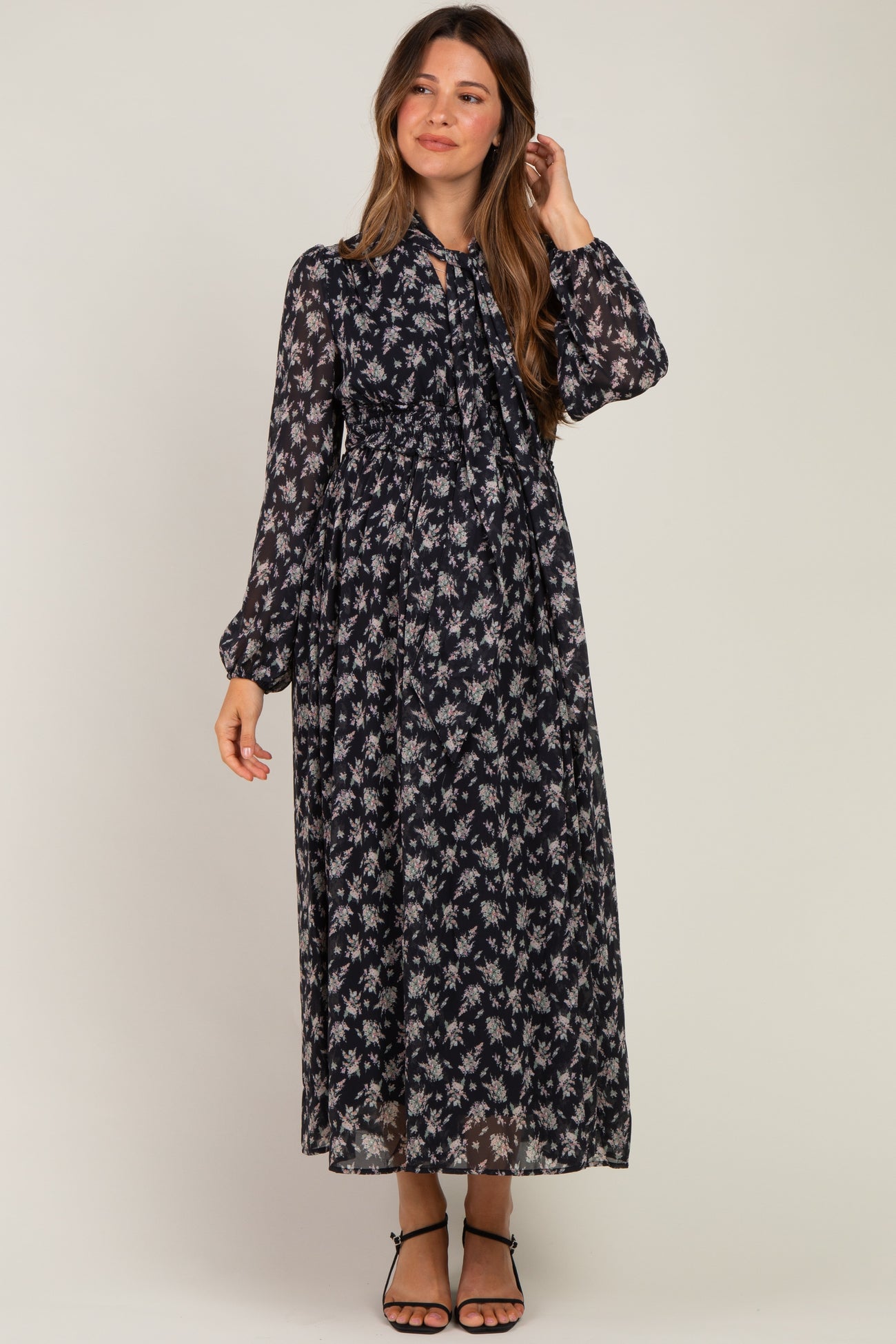woman wearing a floral black maternity maxi dress with long sleeves and a tied neckline, showing her baby bump