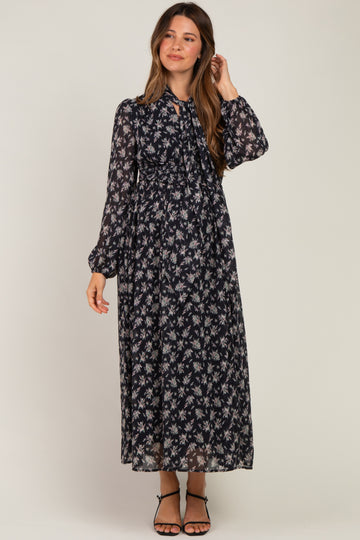 woman wearing a floral black maternity maxi dress with long sleeves and a tied neckline, showing her baby bump