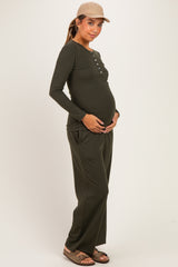 woman wearing a dark green long sleeve maternity top with buttons and matching wide-leg pants, holding her baby bump