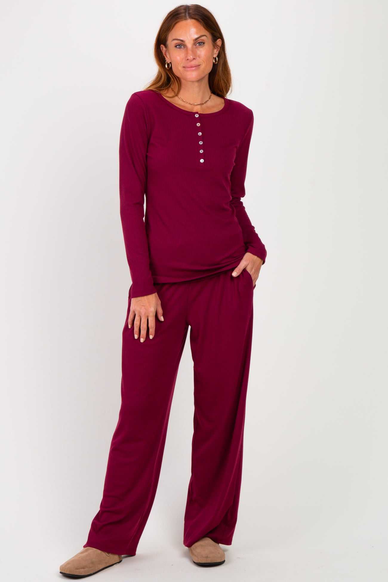 woman wearing a burgundy long sleeve loungewear set with buttons and matching pants, standing hands in pockets