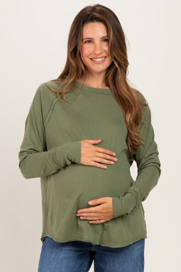 woman wearing a green long sleeve maternity top and holding her baby bump
