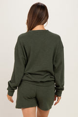 woman wearing a dark green maternity sweatshirt and matching shorts, seen from the back, showing a relaxed fit