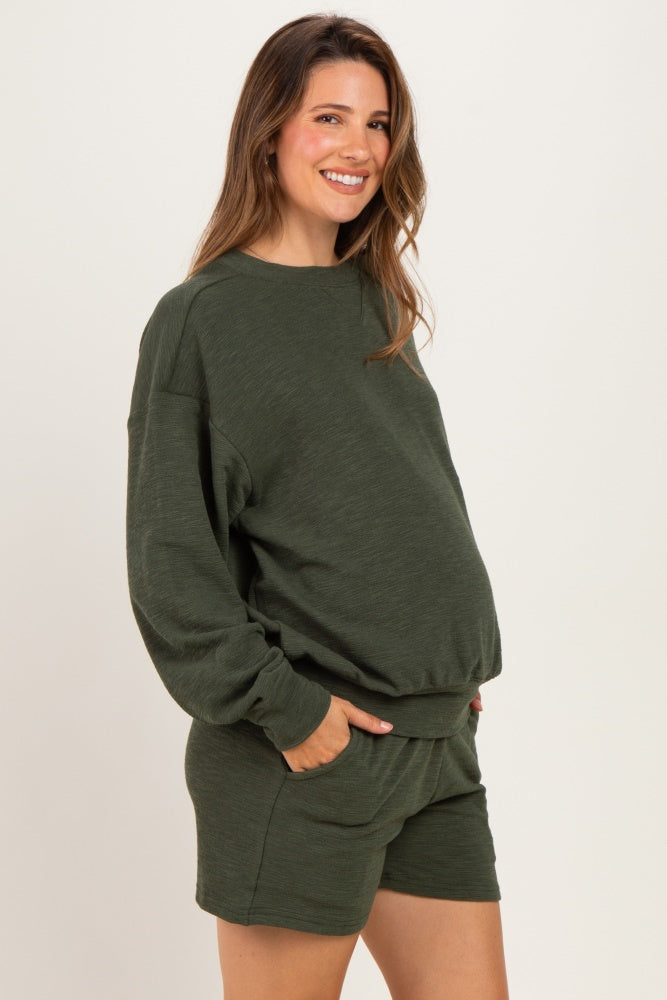 woman wearing a dark green maternity sweatshirt and matching shorts, showing her baby bump with pockets in both garments