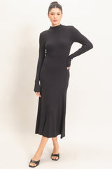 woman wearing a black ribbed long sleeve midi dress with a mock neckline and thumbholes, standing with one foot forward