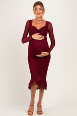 woman wearing a burgundy long sleeve maternity dress with a ruffled hem and holding her baby bump