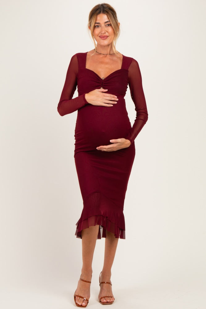 woman wearing a burgundy long sleeve maternity dress with a ruffled hem and holding her baby bump